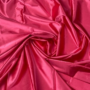 May include: A close-up of a deep pink satin fabric with soft, flowing folds and a smooth, silky texture.