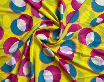 Puede incluir: Tela amarilla con un patrón repetitivo de círculos rosas y azul verdoso superpuestos. La tela está drapeada y doblada.