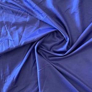 May include: A close-up of a smooth, silky fabric in a deep blue color. The fabric is draped and folded, creating soft curves and folds.