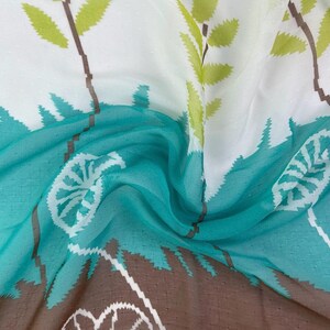 May include: A flowing fabric with a pattern of stylized trees and leaves. The design features a color palette of white, teal, brown, and green. The fabric has a semi-sheer quality, with a subtle dotted texture.
