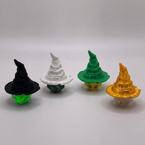 May include: Four different colored dice with a wizard hat design. The dice are green, white, green, and gold. Each die has a different number on each side.