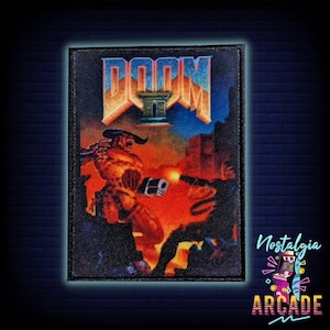 Könnte beinhalten: Ein schwarzer und roter gestickter Patch mit dem Logo des Doom II Videospiels und einer Dämonenfigur. Der Patch hat einen schwarzen Hintergrund mit den Worten "Doom II" in weißen und roten Buchstaben. Die Dämonenfigur ist rot und hat Hörner und einen Schwanz. Der Patch ist von einem schwarzen Rand umgeben.