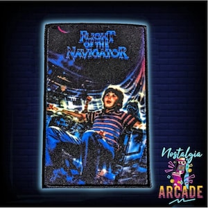 Può includere: Una toppa ricamata nera e blu con un ragazzo in una camicia a righe seduto su un'astronave con il testo "Flight of the Navigator" sopra di lui.