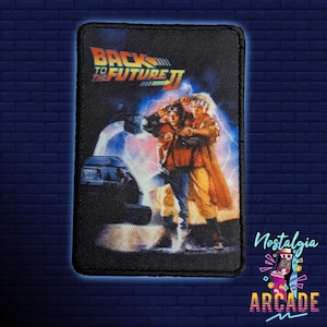 Op de afbeelding: Een zwart-witte patch met de tekst "Back to the Future II" en een scène uit de film met twee personages die voor een auto staan.