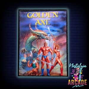 May include: A black and white embroidered patch with the words "Golden Axe" in gold lettering. The patch features a green dragon, a muscular man holding a sword, and a woman in a red and white outfit holding a sword. The patch is surrounded by a black border.