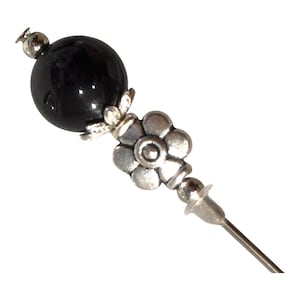 May include: A decorative hat pin with a black, round bead at the top. The pin features a silver-toned flower and a small silver bead. The pin is designed to be inserted into a hat or other fabric.