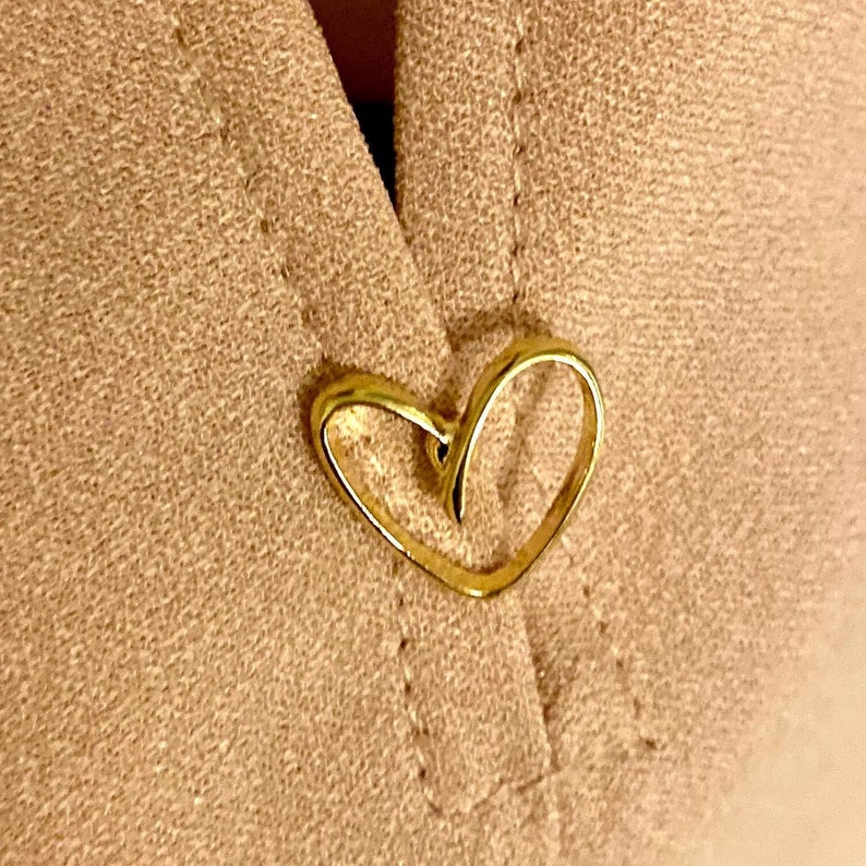 May include: A gold heart-shaped metal button on a brown fabric background.