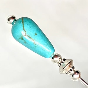 Könnte beinhalten: Eine türkisfarbene Glasperle mit goldenen Flecken und silbernen Akzenten auf einer silbernen Nadel.