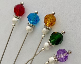 May include: Five colorful glass beads on silver pins. The beads are red, blue, orange, green, and purple.