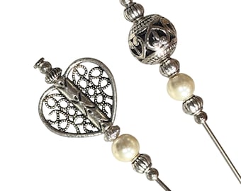 May include: Two silver-coloured hat pins. One has a filigree heart design, the other a decorative sphere. Both have faux pearl accents and are set on long, slender pins. Ideal for adding a touch of elegance to hats or other accessories.