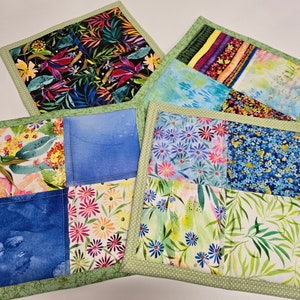 May include: Four handmade quilted pot holders with a green border and a variety of floral and leaf patterns. The pot holders are made with different fabrics, including blue, green, pink, and yellow.