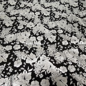May include: Black fabric with a silver floral pattern. The pattern features large hibiscus flowers and smaller floral accents.