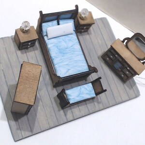 May include: A miniature wooden bedroom set featuring a blue bed, a dresser with a mirror, and two bedside tables. The set is displayed on a grey wooden floor.