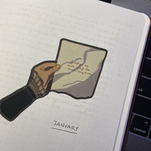 Może przedstawiać: Ręka trzymająca kawałek papieru z tekstem "I still get an exotic range from shalds, sony to say". Papier jest złożony na pół, a ręka ma na sobie czarną rękawiczkę z koronkowym wzorem. Pod ręką widnieje napis "JANUARY".