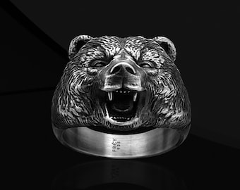 May include: A silver ring with a detailed bear head design. The bear's mouth is open and its teeth are visible. The ring is made of sterling silver and is marked with the word "FREY" and the number "925".