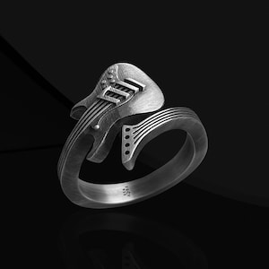May include: A silver ring with a guitar design. The guitar is on the side of the ring and the band is plain.