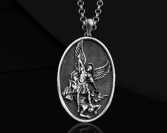 Könnte beinhalten: Ovale Silberanhänger-Halskette mit einem detaillierten Relief eines Engels mit Flügeln, der ein Schwert und eine Waage über einer Figur hält. Der Anhänger hängt an einer Silberkette. Das Design ist vor einem strukturierten Hintergrund.