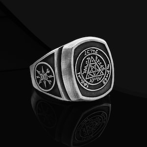 May include: A silver ring with a black and white design. The ring features a triangular symbol with a circle around it and the text "I C T H I" around the circle. The ring also features a smaller symbol on the side.