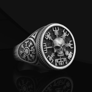 May include: A silver ring with a skull and compass design. The ring features a detailed skull with a compass rose surrounding it. The compass rose is filled with intricate symbols and designs.