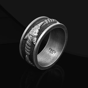 Op de afbeelding: Een zilveren ring met een getextureerd ontwerp met een prikkeldraad- en pijlpuntmotief. De ring is gegraveerd met "FREY 925".
