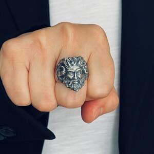 May include: A silver ring with a detailed design of a man's face with a beard and hair. The ring is worn on a person's finger.