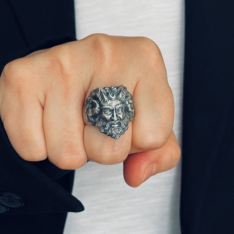 May include: A silver ring with a detailed design of a man's face with a beard and hair. The ring is worn on a person's finger.