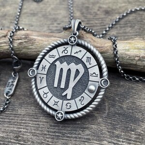 May include: A silver necklace with a round pendant featuring the Virgo zodiac sign surrounded by a circle of all the zodiac signs. The pendant is on a silver chain.