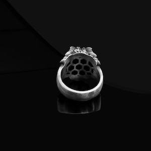 May include: A silver ring with a detailed lion head design. The ring has a honeycomb pattern on the back.