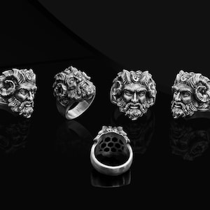 May include: Five silver rings with a detailed design of a man's face with horns and a beard. The rings are displayed on a black surface.