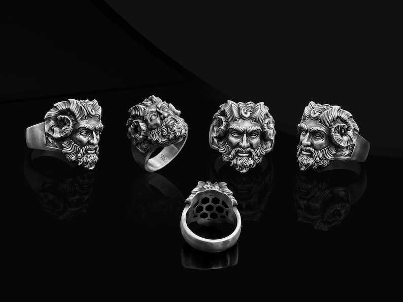 May include: Five silver rings with a detailed design of a man's face with horns and a beard. The rings are displayed on a black surface.