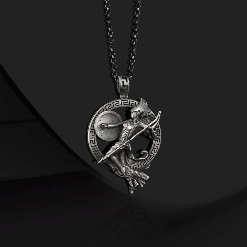 May include: Silver necklace with a pendant featuring a Greek goddess holding a spear and shield, surrounded by a circle with a Greek key design.