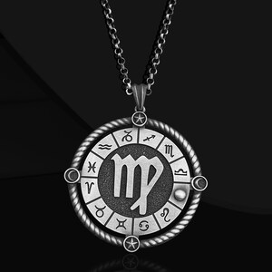 May include: Silver necklace with a round pendant featuring the Virgo zodiac sign surrounded by the other zodiac signs. The pendant has a textured, aged look.