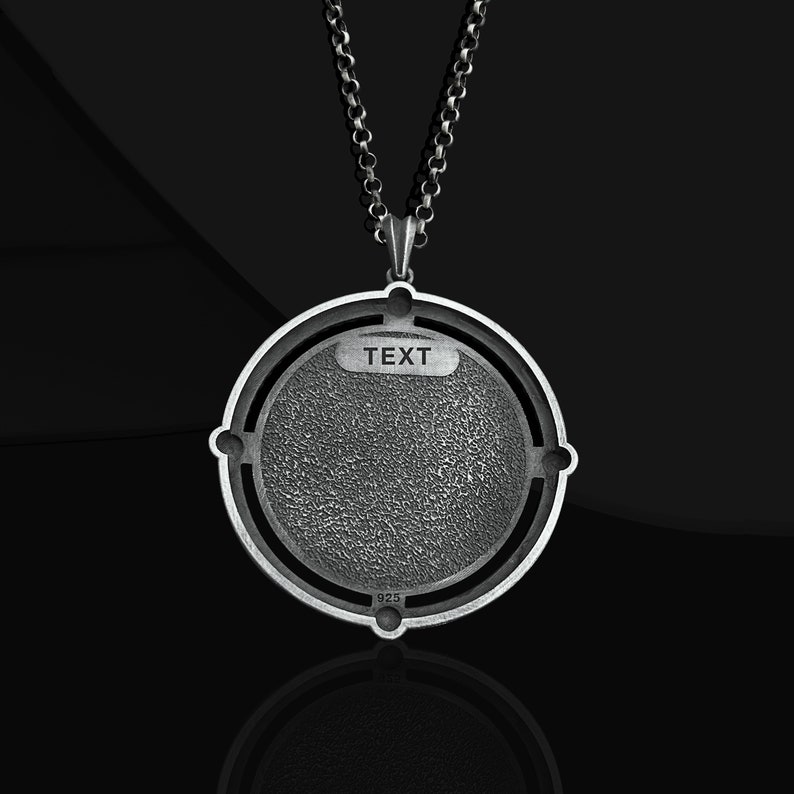 May include: A silver necklace with a round pendant featuring a textured surface and the word "TEXT" inscribed on it. The pendant is marked with "925" on the back.