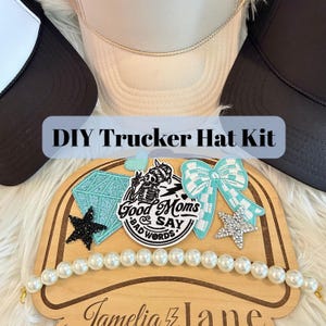 May include: A DIY trucker hat kit featuring three hats in black and beige, accompanied by a wooden display board. The board holds a circular patch with the text Good Moms Say Bad Words, a diamond patch, a bow patch, two star patches, and a pearl chain.