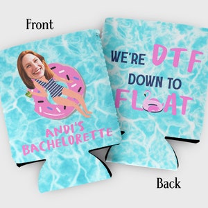 May include: A blue and white can cooler with a pink donut float and a woman's face in the pool. The text on the front says "Andi's Bachelorette". The text on the back says "We're DTF Down to Float".