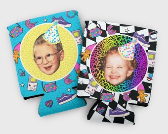 May include: Two colorful can coolers with a retro 90s theme. Each cooler features a photo of a child wearing a party hat, surrounded by a circle of colorful patterns. One cooler has a blue background with stars and a gameboy, while the other has a black and white checkered background with a leopard print circle.