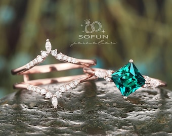Könnte beinhalten: Ein Ring aus Roségold mit einem quadratischen smaragdgrünen Edelstein und ein passender Ring aus Roségold mit einem geschwungenen Design und kleinen Diamanten.
