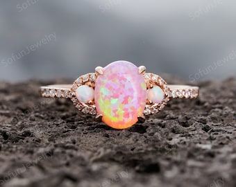 May include: A rose gold engagement ring with a large oval pink opal gemstone surrounded by smaller white opal gemstones and a band of small diamonds.