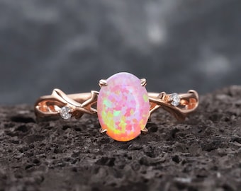 May include: A rose gold ring with a pink opal gemstone and two smaller clear gemstones set in a delicate branch design.
