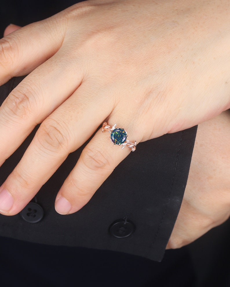 May include: A rose gold ring with a green and black opal stone set in a delicate leaf design.