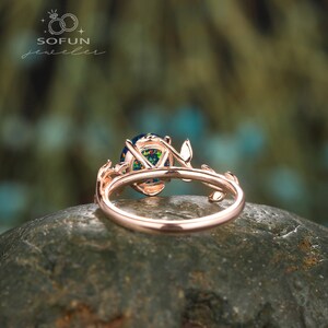 May include: A rose gold ring with a large oval opal gemstone set in a delicate branch design. The ring is on a gray rock.