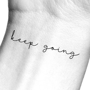 Pode incluir: Um close-up de um pulso com uma tatuagem tempor&aacute;ria que diz "keep going" em uma fonte de escrita manuscrita simples.