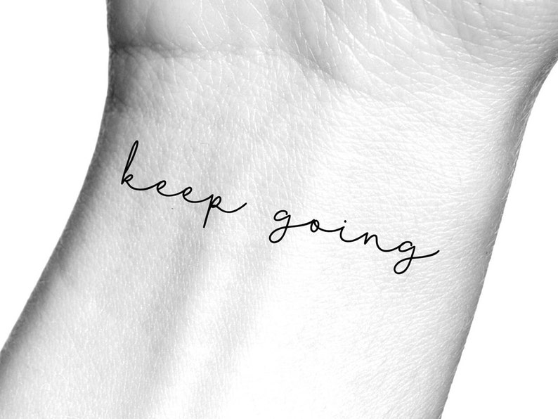Pode incluir: Um close-up de um pulso com uma tatuagem tempor&aacute;ria que diz "keep going" em uma fonte de escrita manuscrita simples.