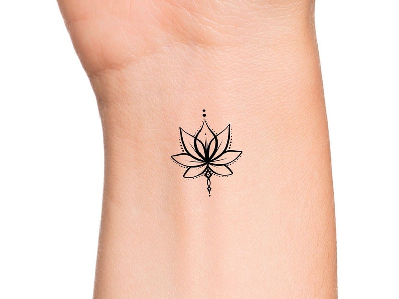 May include: A simple black line drawing of a lotus flower tattoo on a person's wrist.