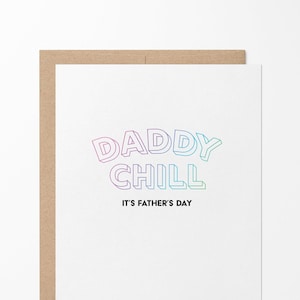 May include: A white greeting card with a brown envelope behind it. The card features the text DADDY CHILL in a 3D-style gradient font transitioning from pink to blue and green, with the black text IT'S FATHER'S DAY printed directly below it.