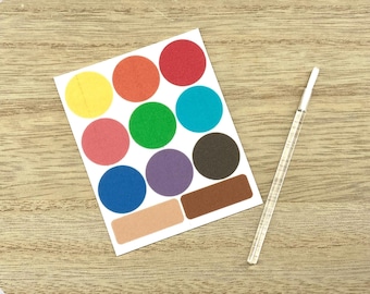 May include: A sheet of colorful round stickers in various colors, including red, orange, yellow, green, blue, and purple. Also included are two rectangular stickers and a clear plastic stick. The stickers are on a white background, placed on a wooden surface.
