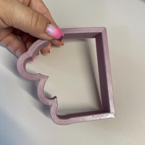 Op de afbeelding: Een lichtroze plastic koekjesvormpje in de vorm van een rechthoek met een gegolfde bovenrand.