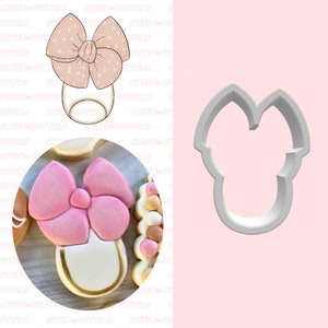 May include: A cookie cutter in the shape of a baby's onesie with a bow on top. The cutter is made of metal and is silver in color.
