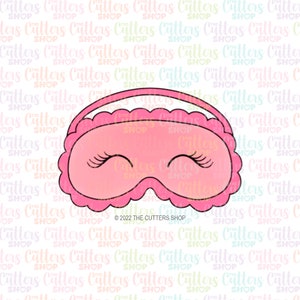 May include: Pink sleep mask with eyelashes and a scalloped edge. The mask has a white elastic band.