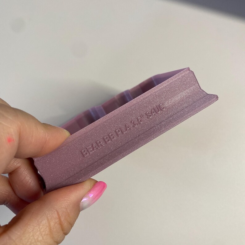 Op de afbeelding: Een close-up van een roze plastic koekjesvormpje met de woorden "BEAR BEAR" en "SAUC" erop gegraveerd.